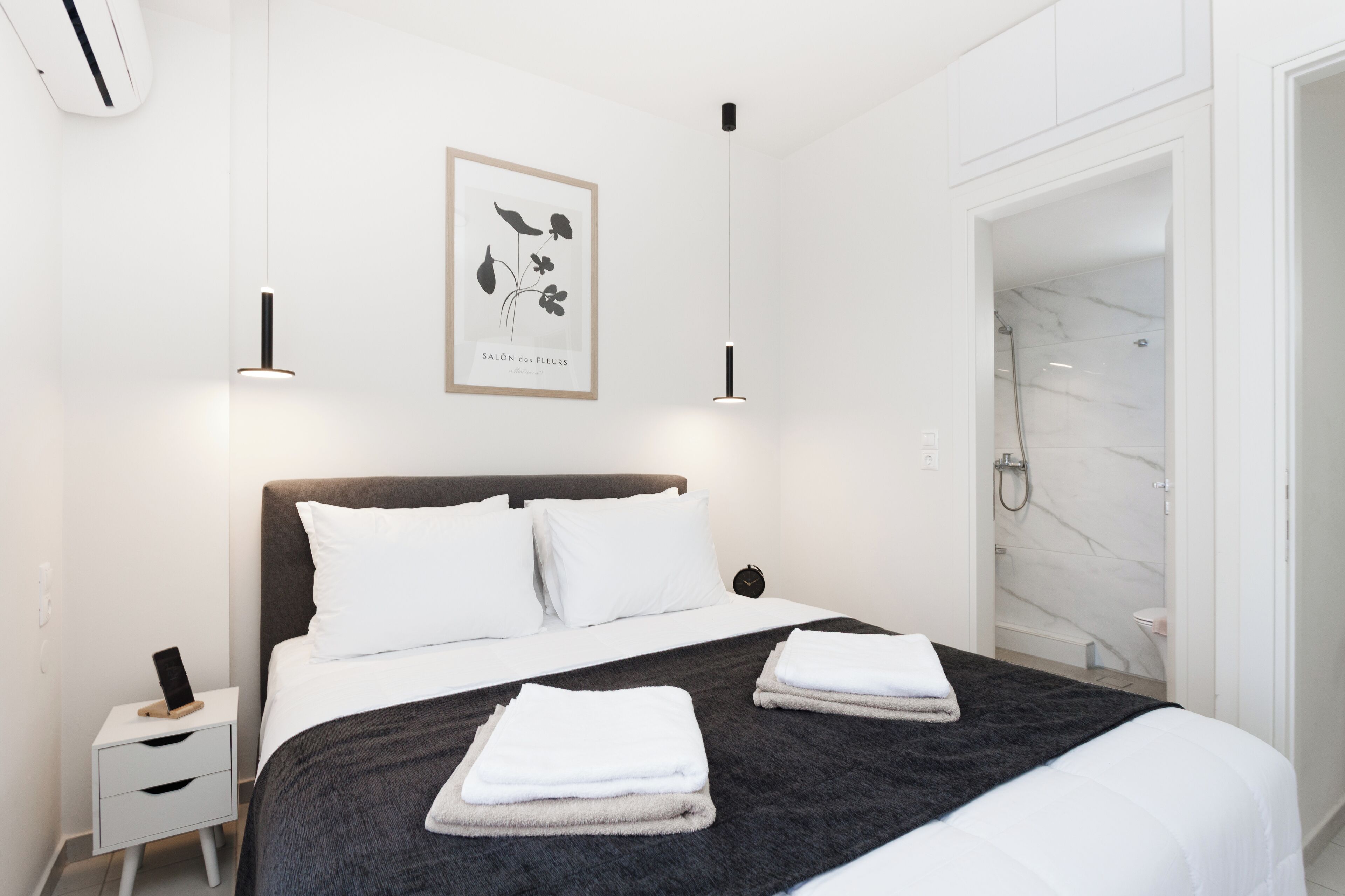 Een moderne hotelkamer met een groot bed, een nachtkastje, een ingelijste botanische print en een badkamer met een marmeren douche.