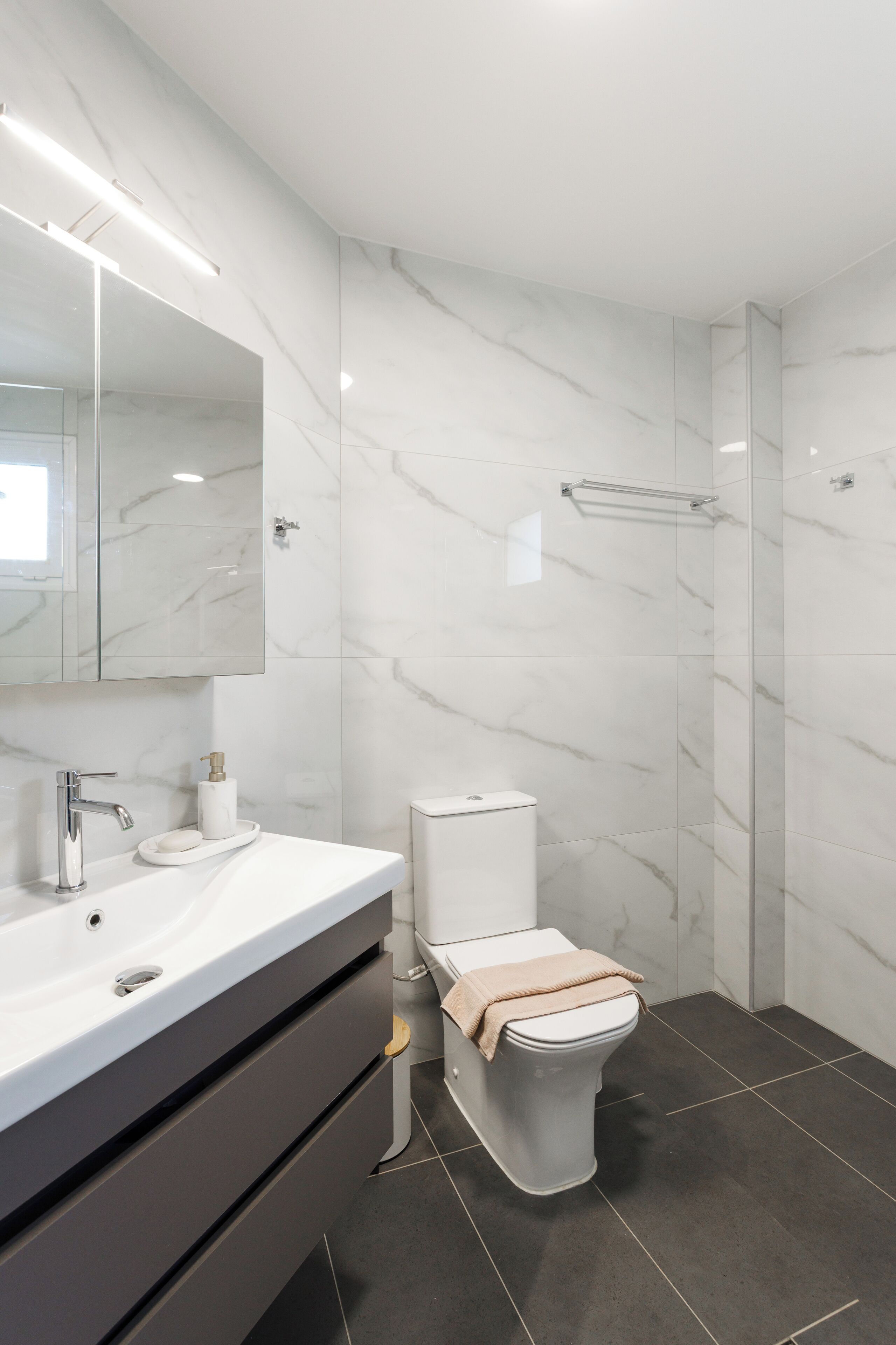 A modern bathroom with a marble wall, a white sink, a toilet, and a shower area.