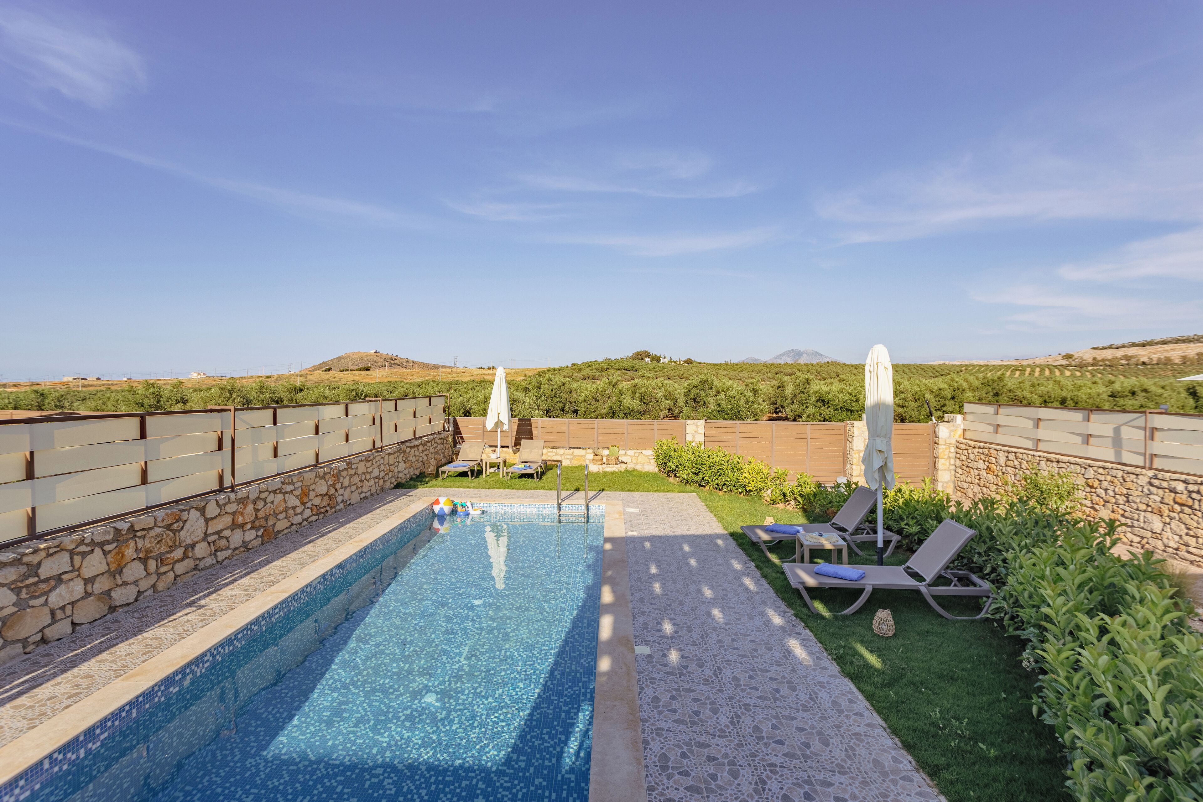 A swimming pool with lounge chairs and umbrellas, surrounded by stone walls and greenery.