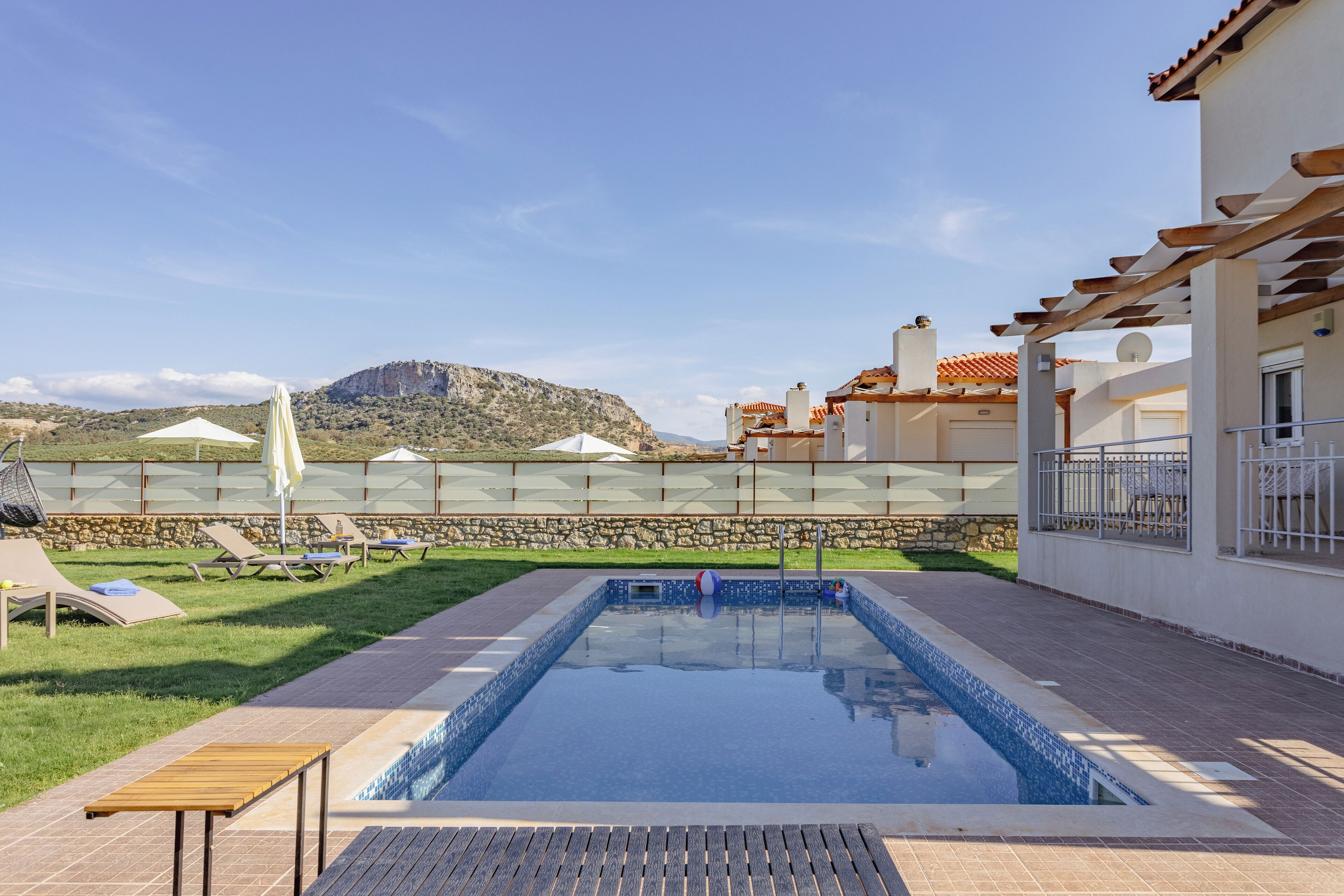 En pool med en kant av sten, solstolar och en pergola.