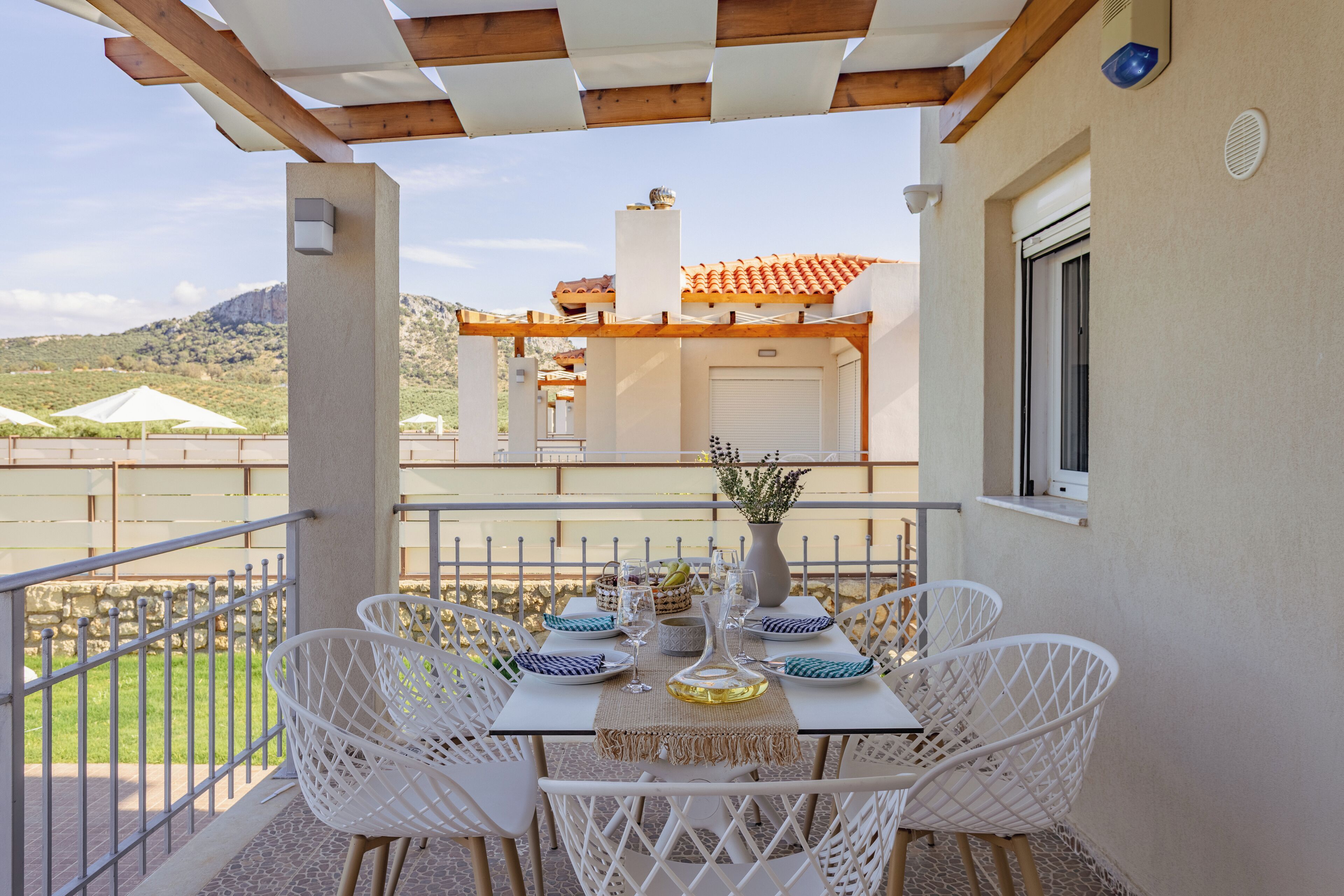 Eine Terrasse mit Esstisch, weißen Stühlen und Blick auf ein Gebäude mit Ziegeldach.