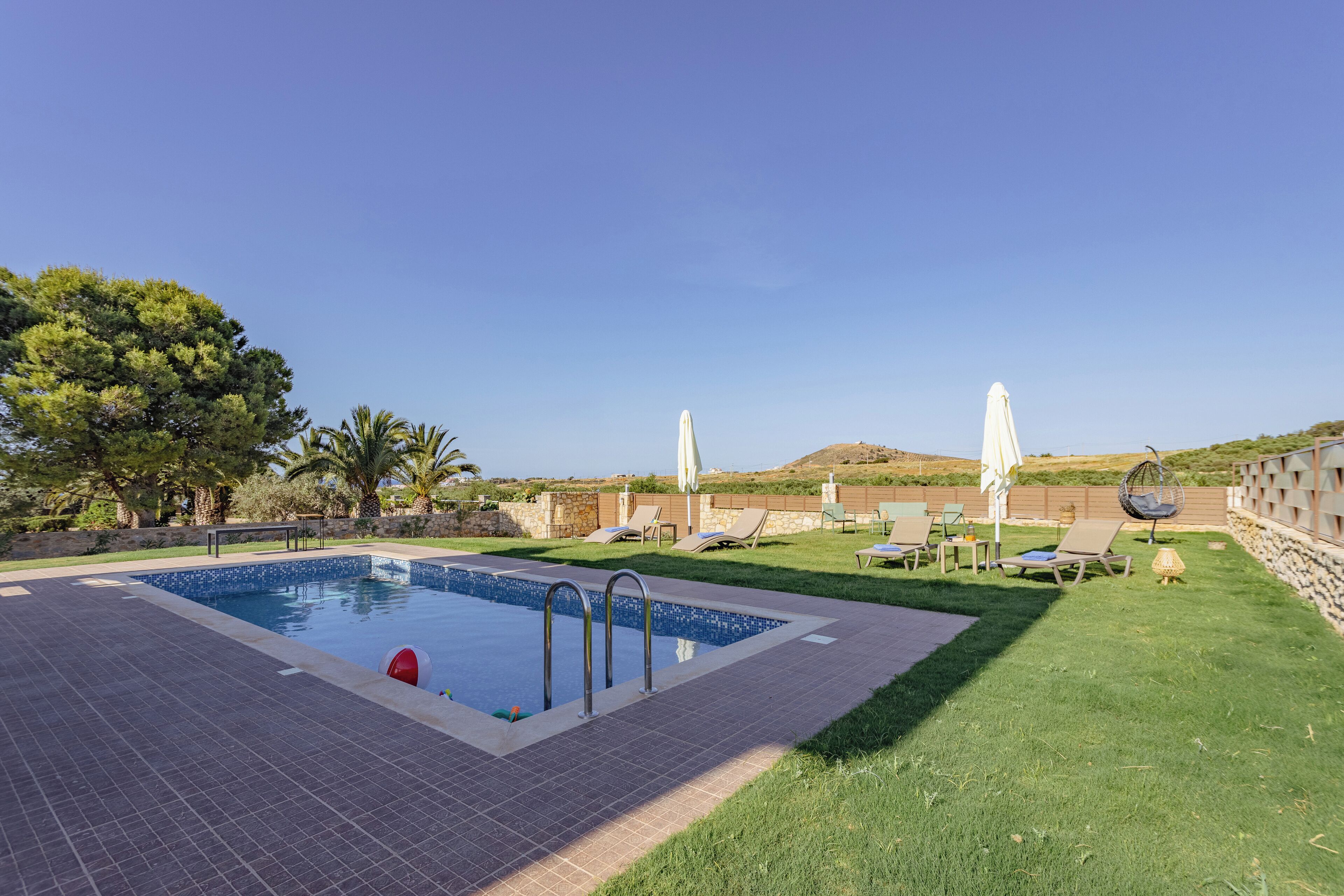 Una piscina con bordes azulejados, rodeada de césped con sillas de descanso y sombrillas.