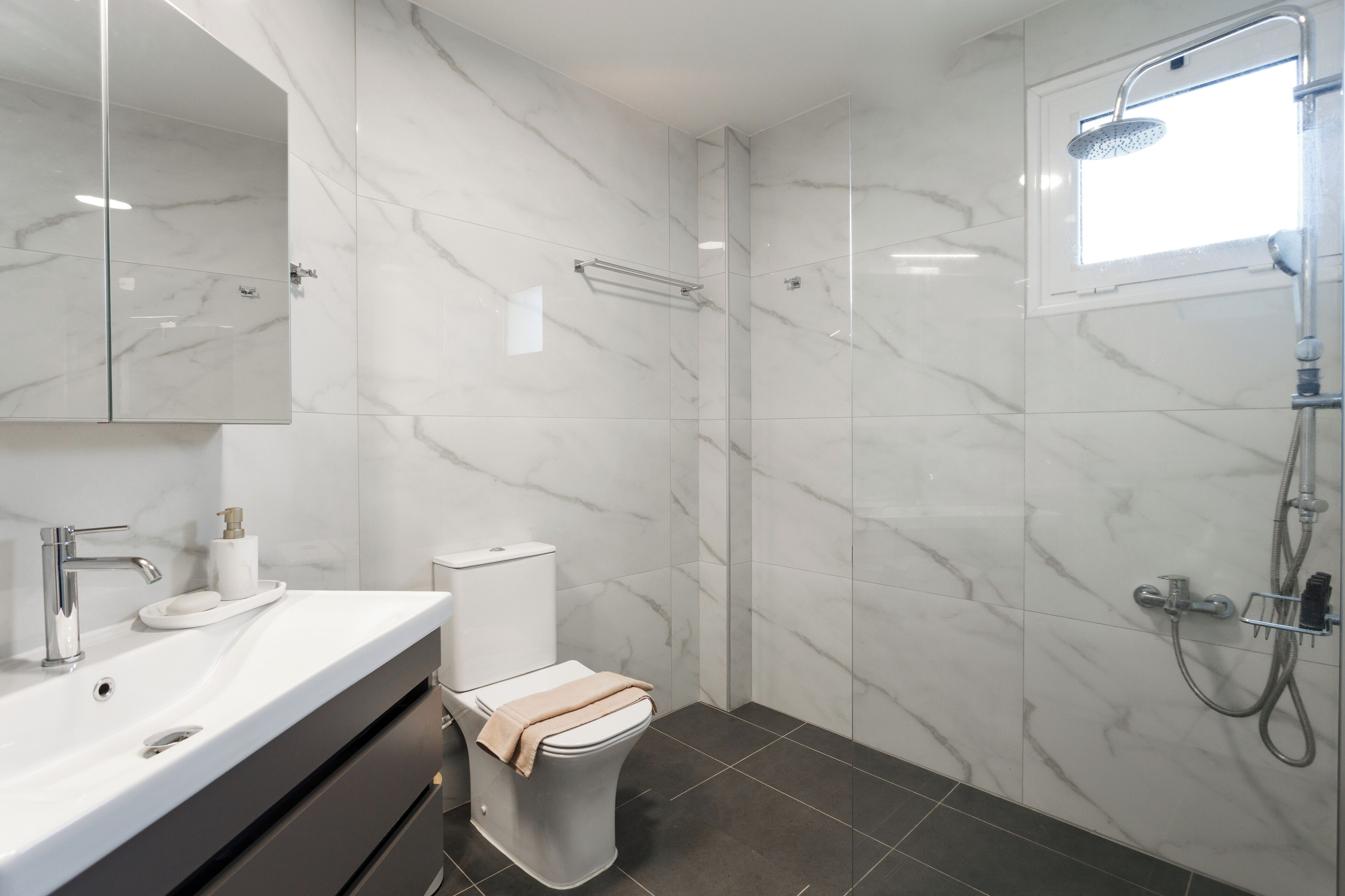 A modern bathroom with a marble vanity, a toilet, a shower, and a large mirror.
