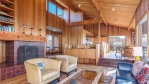 A spacious living area with a fireplace, wooden bookshelves, a dining area, and a kitchen. - Sea Ranch Oceanfront 3BR | Hot Tub | Sleeps 6 (Sea Ranch)