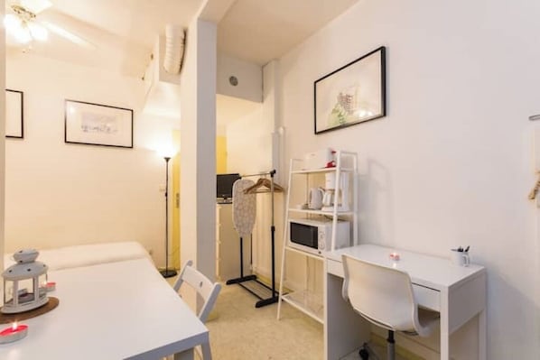 A modern, well-lit room with a white desk, chair, and a hanging clothes rack. There is a framed picture on the wall and a small table with a lantern.