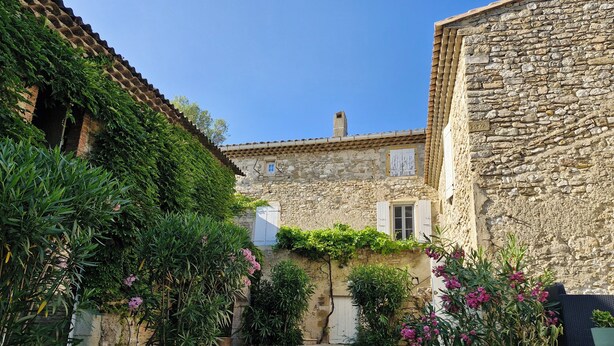 A stone building with a tiled roof and a small garden area with various plants and flowers.