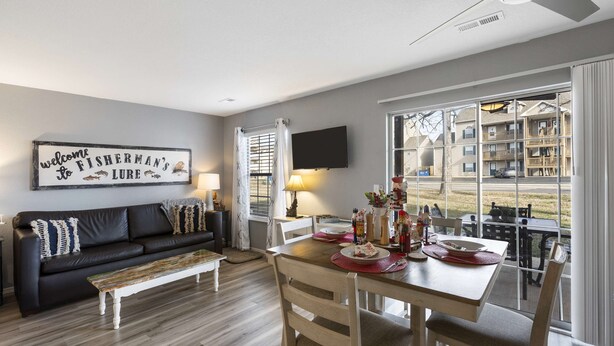 A modern living room with a black leather sofa, wooden dining table, and a large window offering a view of a residential area. - Fisherman's Lure (Branson)