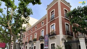 Un edifici històric amb façana vermella, diversos balcons i una estàtua al davant.