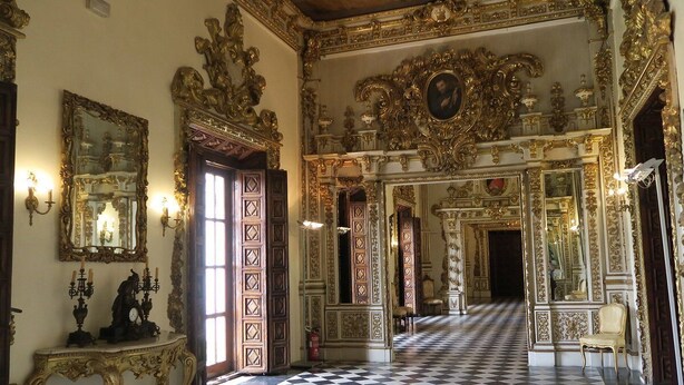Una estança ornamentada amb un paviment de pissos, decoracions daurades elaborades i un gran mirall.