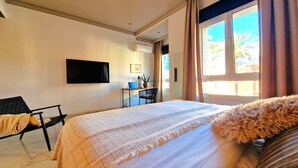 Una habitació d'hotel amb un llit, un escriptori amb un ordinador portàtil, una cadira, un televisor fixat a la paret i una finestra amb cortines.