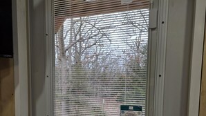 Une porte blanche avec une fenêtre ornée de stores horizontaux, un interphone et un panneau indiquant la présence d’un système de sécurité.