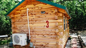 Une cabane en bois avec une plaque portant le numéro 3, un appareil de climatisation et un parterre de fleurs devant.