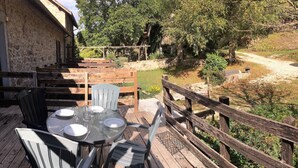 An outdoor dining area with a round table and chairs, surrounded by a wooden deck and a stone wall. - Domaine de Clarat, Béalière gîte in the heart of green Ardèche (Lafarre)