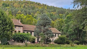 A stone house with a tiled roof, surrounded by lush greenery and a field. - Domaine de Clarat, Béalière gîte in the heart of green Ardèche (Lafarre)