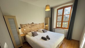 A neatly made bed with pillows, a wooden headboard, a bedside table with a lamp, and a window with curtains. - Domaine de Clarat, Béalière gîte in the heart of green Ardèche (Lafarre)