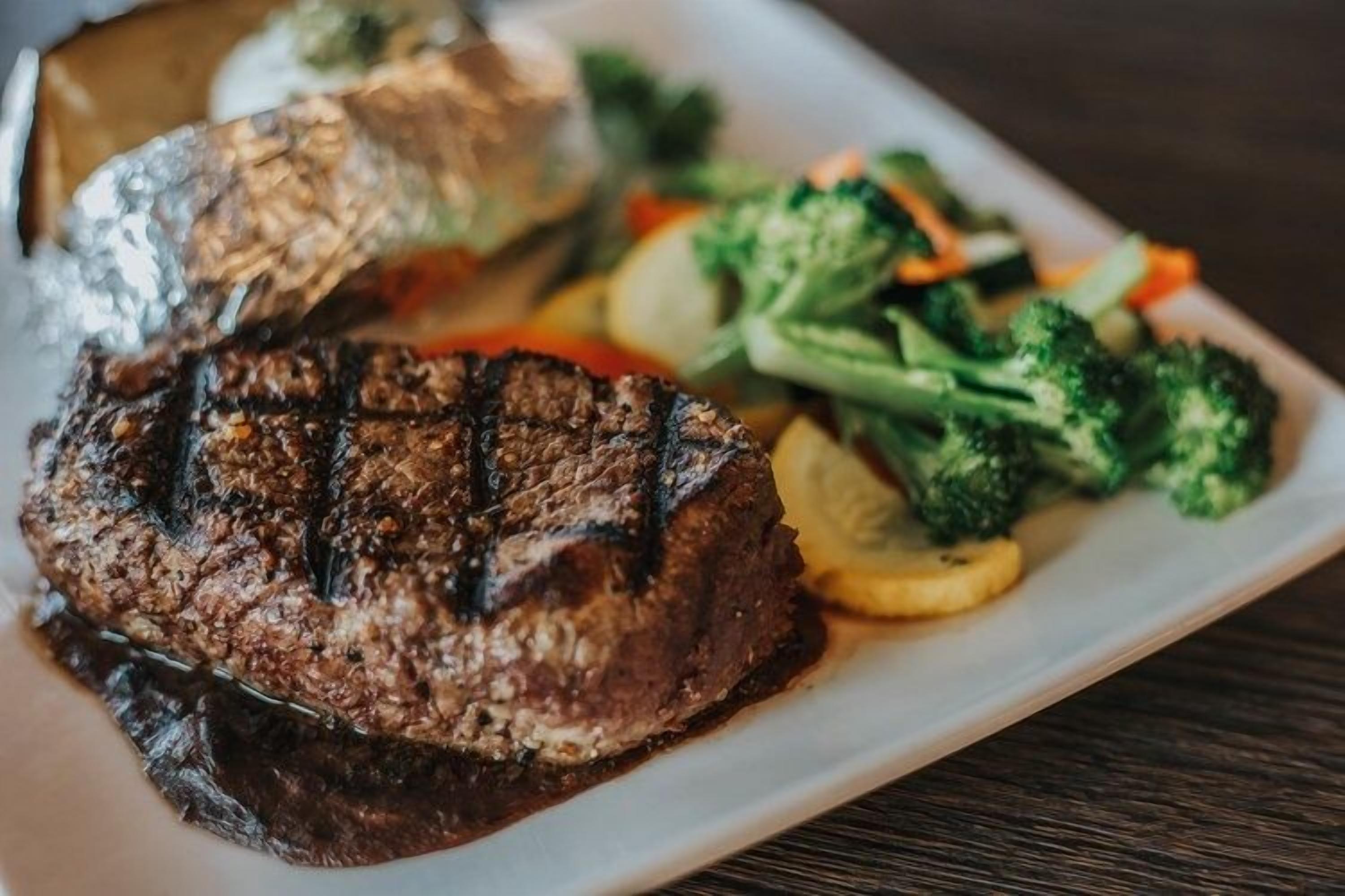 A plate with grilled steak, vegetables, and a piece of fish.