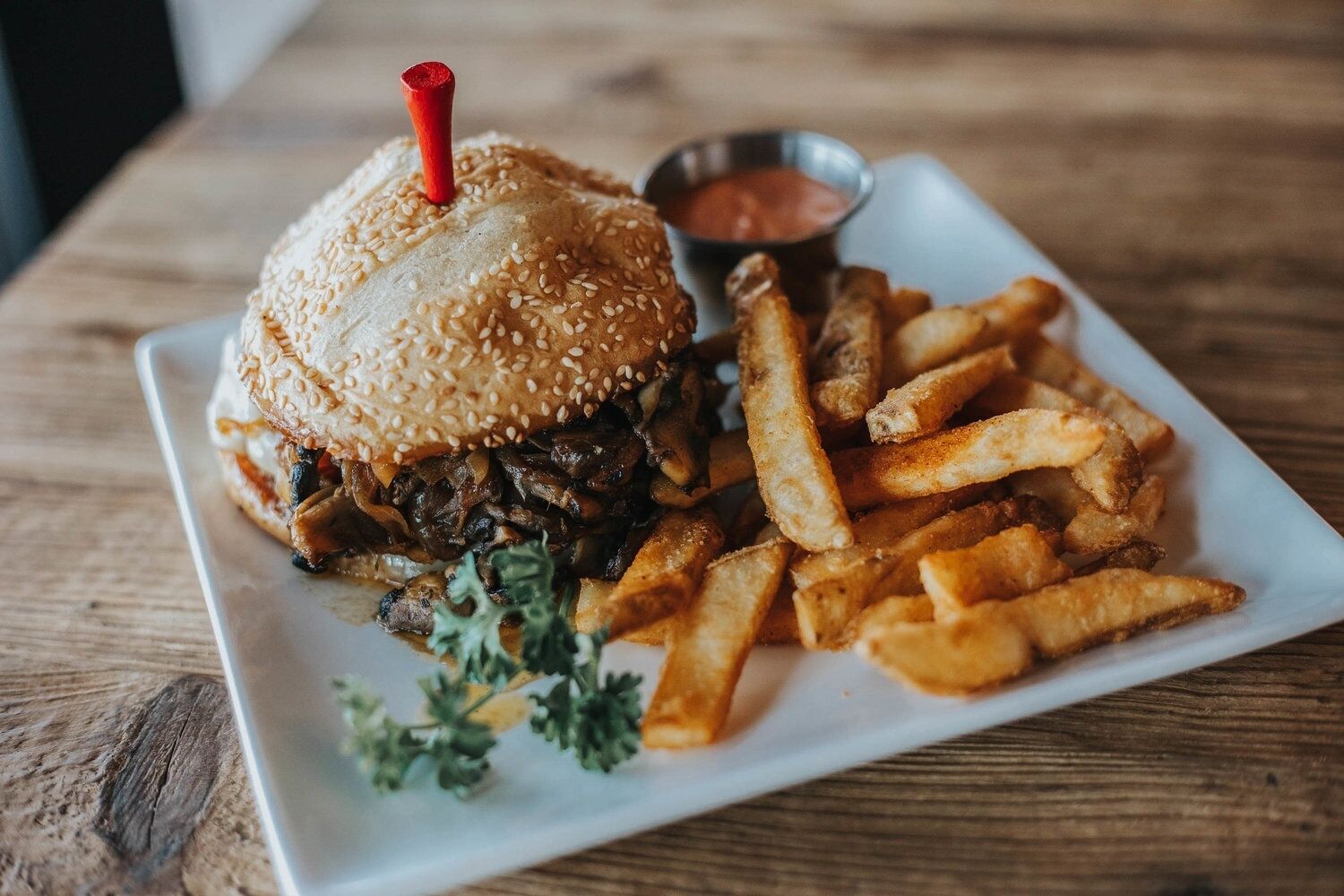 Ein Teller mit einem Sesambrötchen-Burger, Pommes und einer kleinen Sauce.