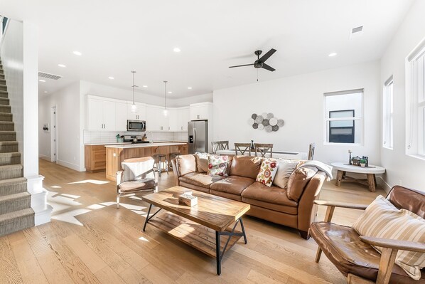 A spacious living area with a wooden coffee table, leather sofa, and a kitchen in the background.