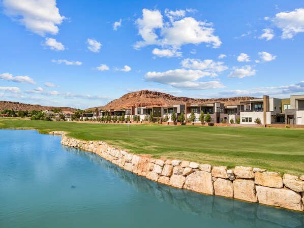 A golf course with a large pond, modern buildings, and a mountain in the background. - Villa #22 At Bloomington Country Club - Fairway To Heaven 3 Bedroom Condo (St. George)