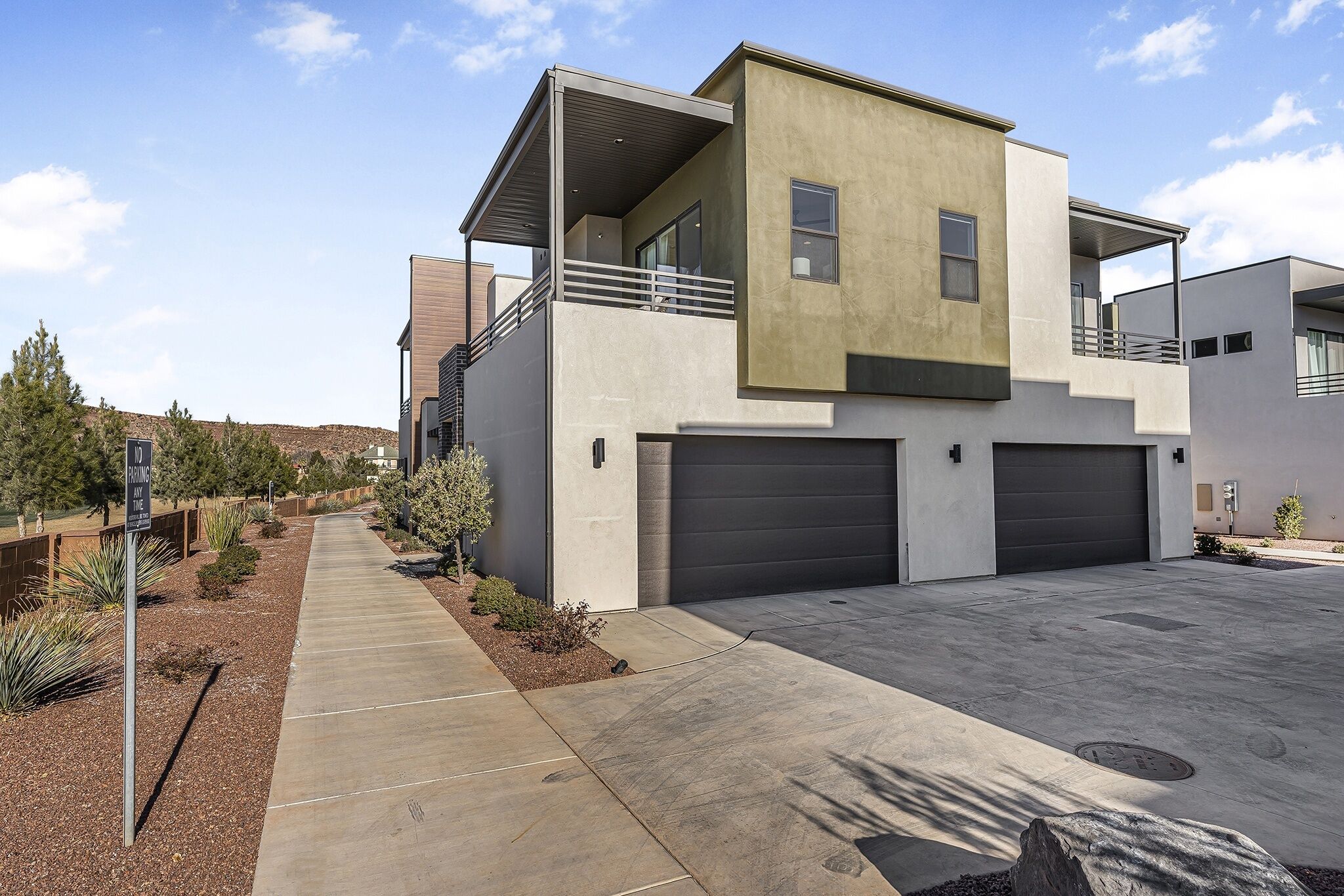 A modern two-story house with a covered balcony, a garage, and a landscaped driveway.
