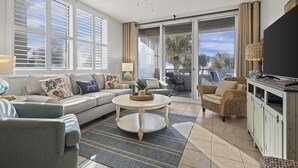 A spacious living room with a sofa, armchairs, a coffee table, and a television.