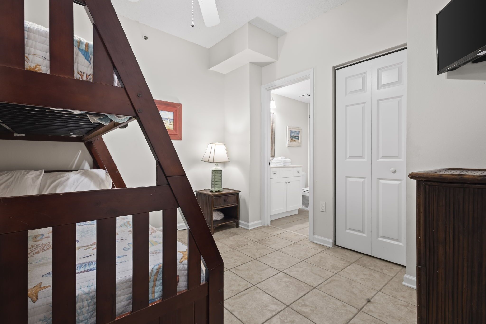 A bedroom with a wooden crib, a nightstand with a lamp, a white bathroom with a toilet, and a closed door.