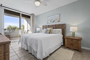 A bedroom with a large bed, two bedside tables with lamps, a ceiling fan, a painting on the wall, and a view of the outdoors through a sliding door. - The Beach Club Bristol 201 3 Bedroom Condo (Gulf Shores)