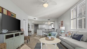 A spacious living room with a large flat-screen TV, a sofa, a coffee table, and a dining area with chairs.