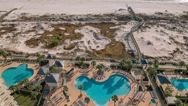 An aerial view of a resort with multiple swimming pools, a beach, and a rocky landscape.
