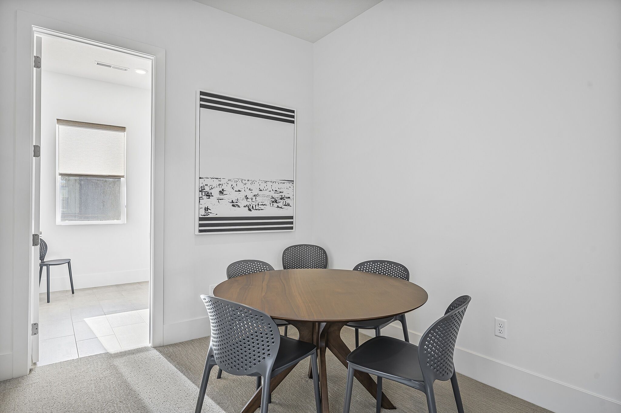 A room with a round wooden table surrounded by four chairs, a white door, and a framed picture on the wall.