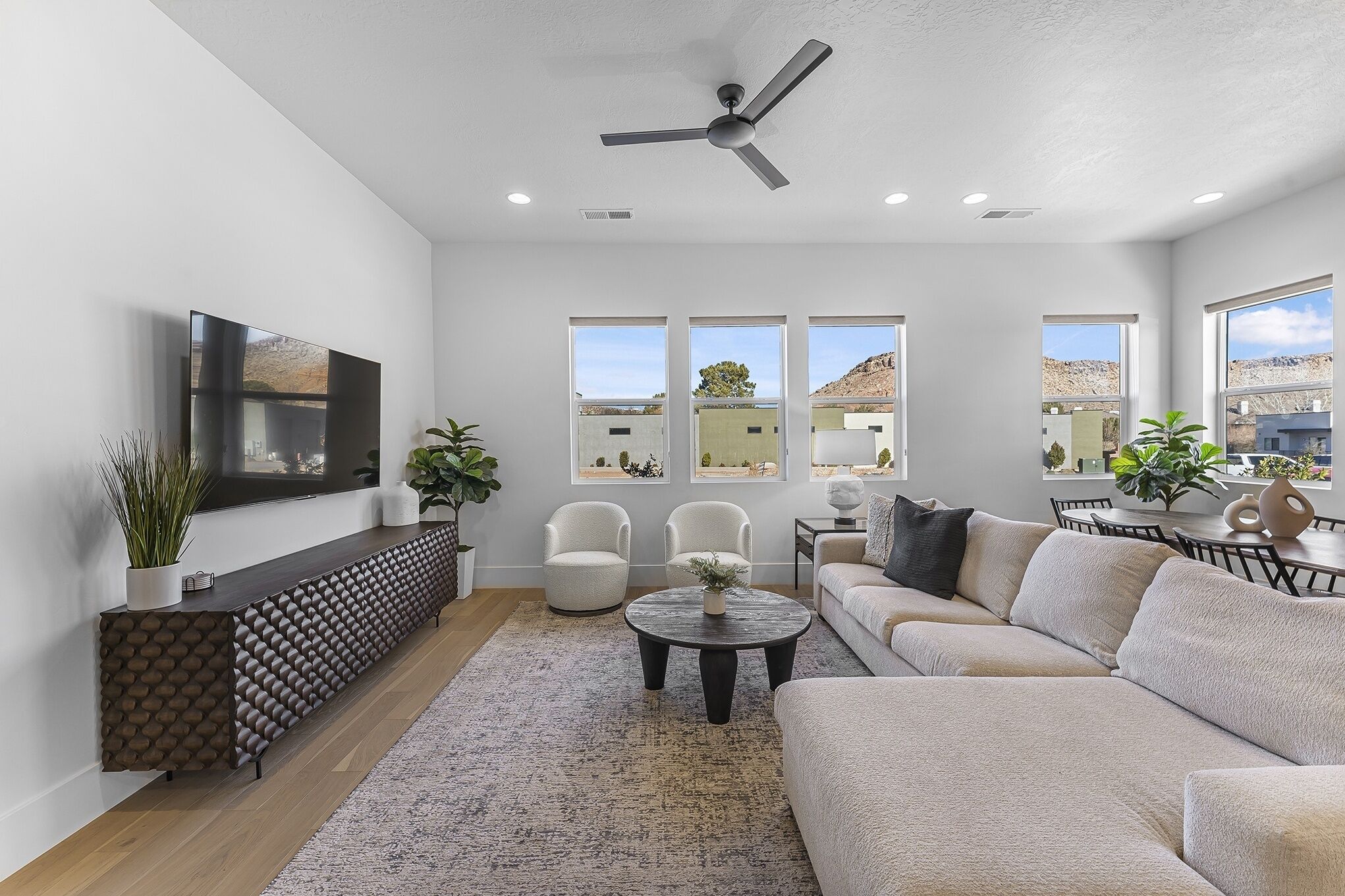 A modern living room with a flat-screen TV, a ceiling fan, and a large window overlooking a mountainous landscape.