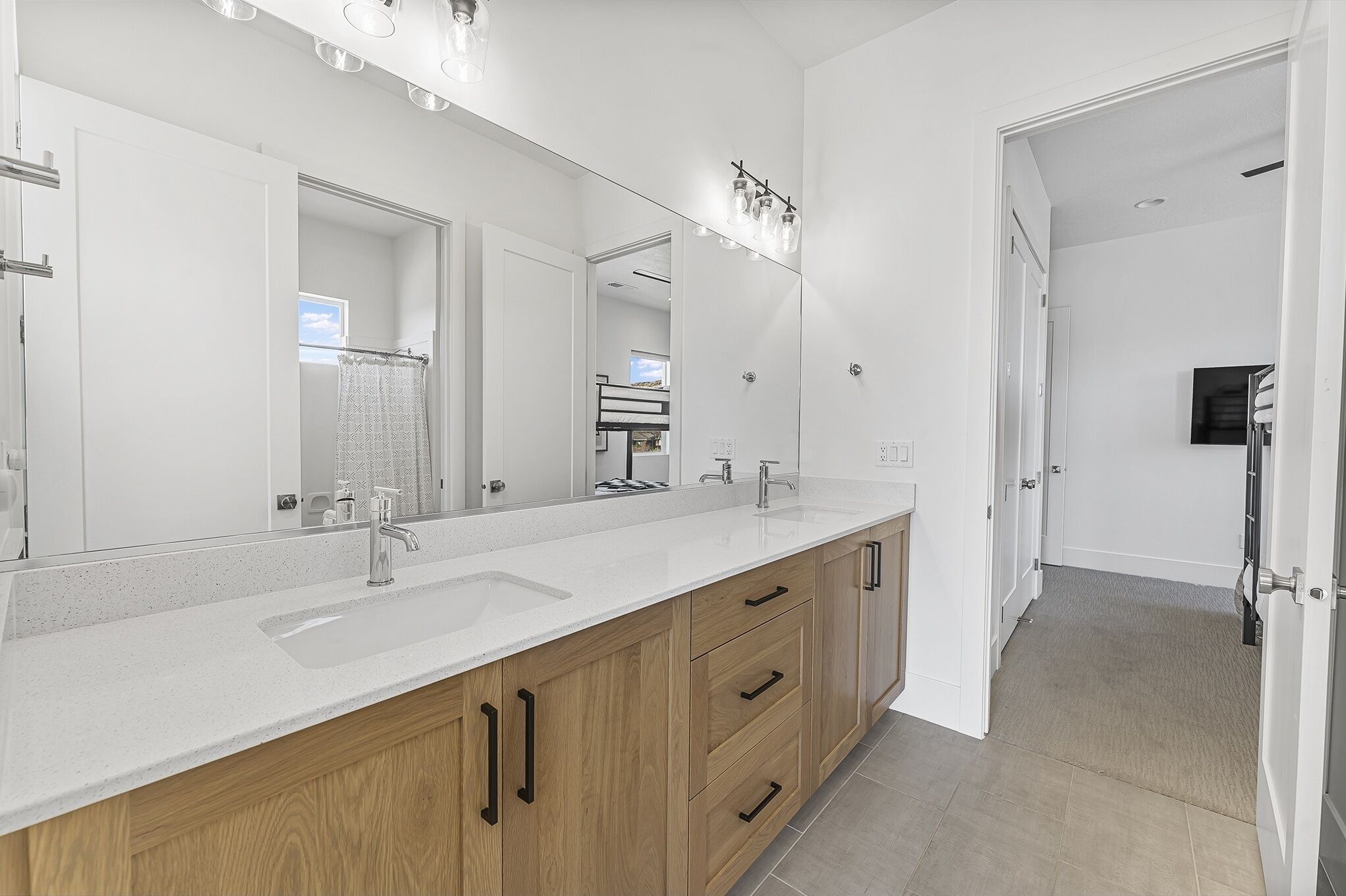Une salle de bain moderne avec un grand miroir, deux vasques, des meubles en bois et un espace douche.