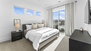 Un dormitorio moderno con cama, mesitas de noche, ventilador de techo y vistas al exterior.