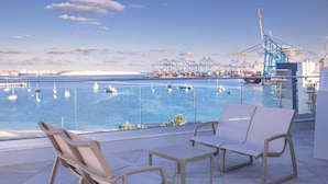 Terraza con dos sillones de descanso con vista a un puerto deportivo con barcos y grúas.