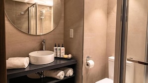 Un baño moderno con un espejo redondo, un lavabo, un inodoro y una cabina de ducha de vidrio.