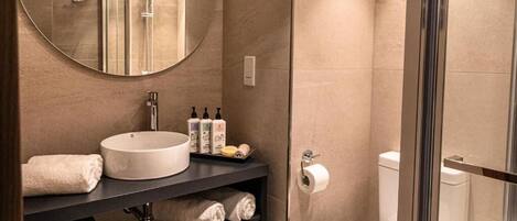 A modern bathroom with a round mirror, a sink, a toilet, and a glass shower enclosure.