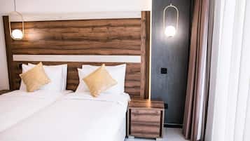 Una habitación de hotel moderna con cabecera de madera, una cama grande con sábanas blancas, dos mesitas de noche y una lámpara colgante.