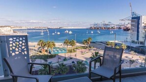 A balcony with two chairs and a small table, overlooking a marina with boats and a port in the background. - CA Sand Dune Hotel (Birzebbuga)