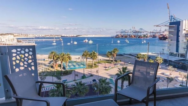 Un balcón con dos sillas y una mesita pequeña, con vista a un puerto deportivo con barcos y un muelle al fondo.