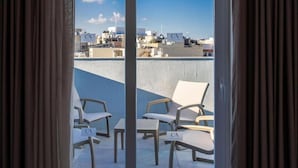 Un balcón con dos sillones de descanso y una pequeña mesa, con vistas a un paisaje urbano con edificios identificados como 'CA'.