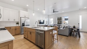Una cocina moderna con una isla central, electrodomésticos de acero inoxidable, armarios de madera e iluminación colgante.