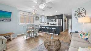 A modern kitchen with a central island, bar stools, and a dining area with a bench and chairs. - Family Tides 107 3 Bedroom Condo (Miramar Beach)