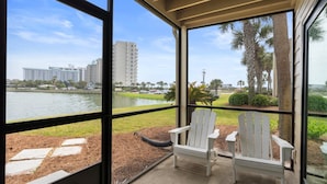 A balcony with two white Adirondack chairs, a view of a lake, and a distant building. - Family Tides 107 3 Bedroom Condo (Miramar Beach)