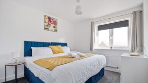 Una habitación de hotel con cama, mesita de noche, ventana con cortinas y una obra de arte colgada en la pared.