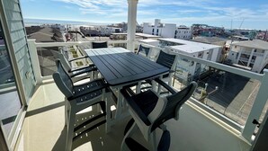 A balcony with a table and chairs, overlooking a coastal area with buildings and a clear sky.