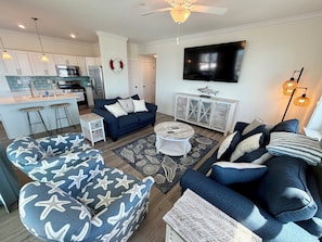 A modern living room with a dark blue sofa, a round coffee table, and a kitchen area with white cabinets and a stainless steel refrigerator. - Southview Condominiums unit 404 Wildwoods Newest Building with a private pool (Wildwood)