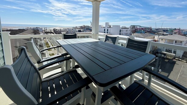 A balcony with a table and chairs, overlooking a coastal cityscape with buildings and a beach.