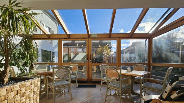 A conservatory with a glass ceiling, wicker furniture, and a potted plant. - ARRIVEL Hotel am Bergson (Munich)