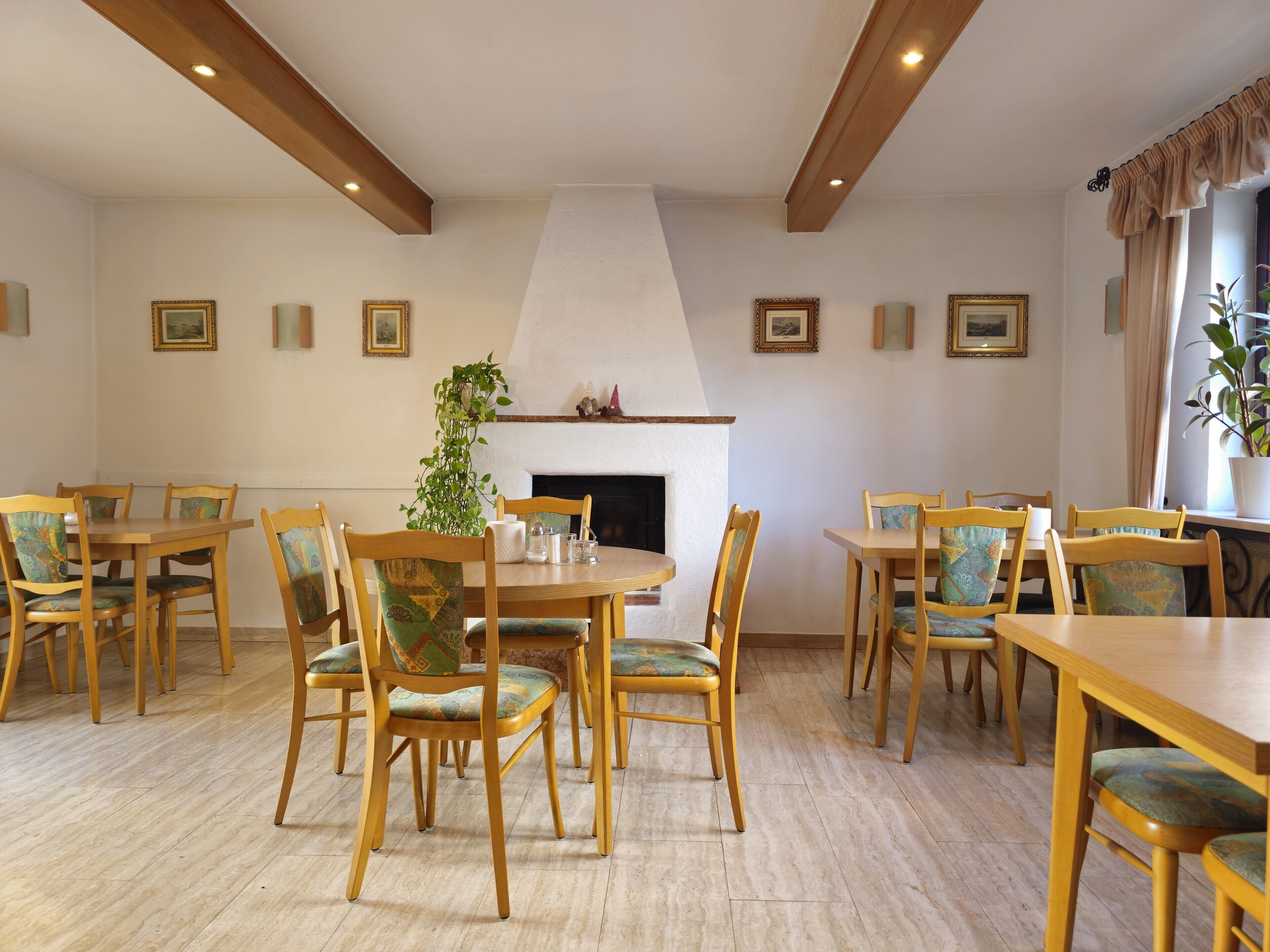 A dining area with wooden tables and chairs, a fireplace, and framed pictures on the walls.