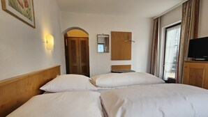 A hotel room with two beds, a wooden headboard, a wall-mounted TV, and a window with curtains. - ARRIVEL Hotel am Bergson (Munich)